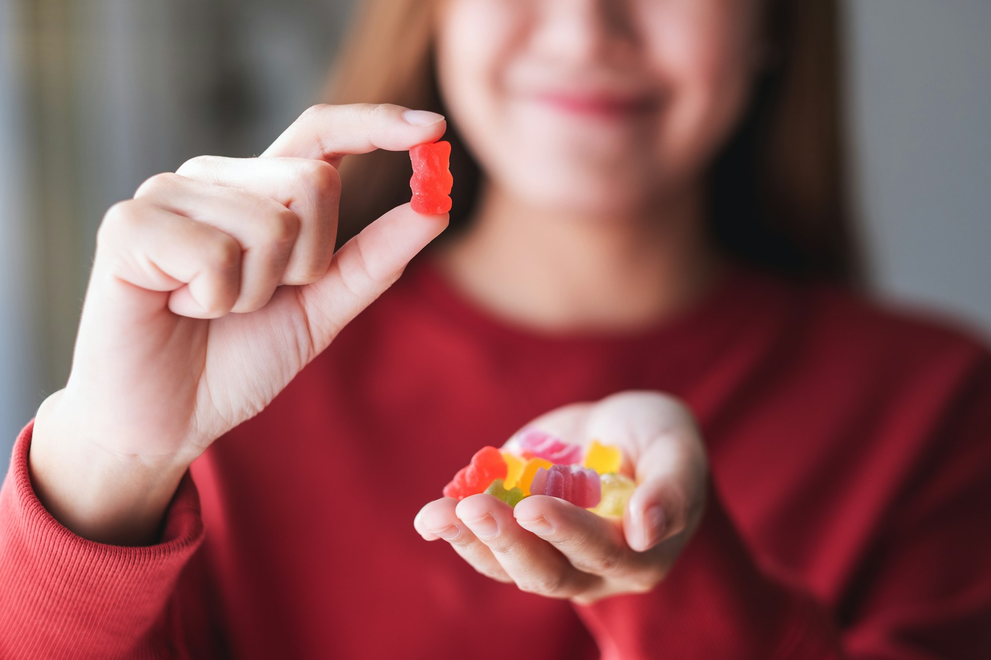 Closeup image of a young woman holding and showing at a red jelly gummy bears